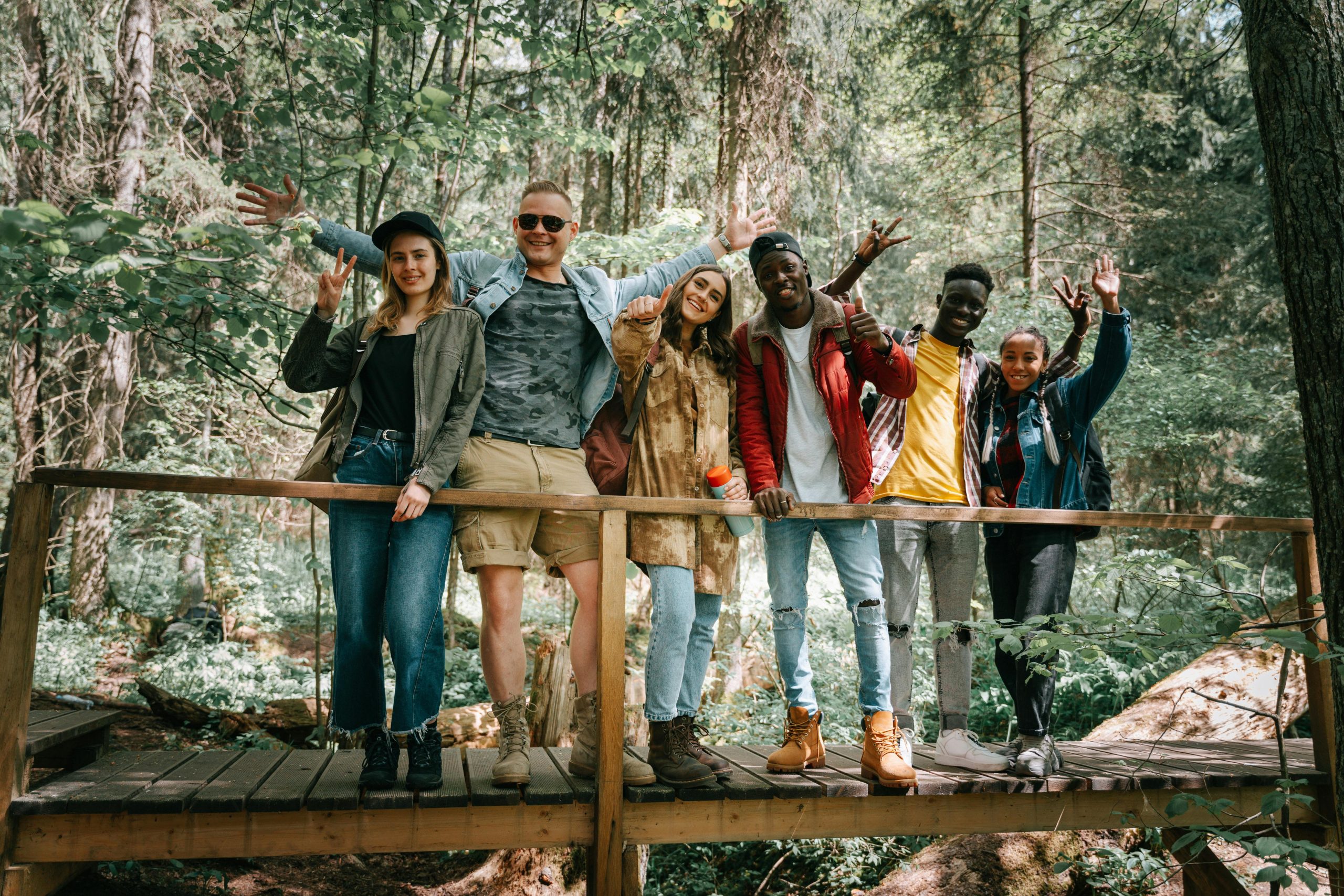 A diverse group of friends hiking and enjoying nature on a wooden bridge in a lush forest.