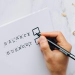 A hand checking balance or burnout on a checklist, symbolizing life balance decisions.