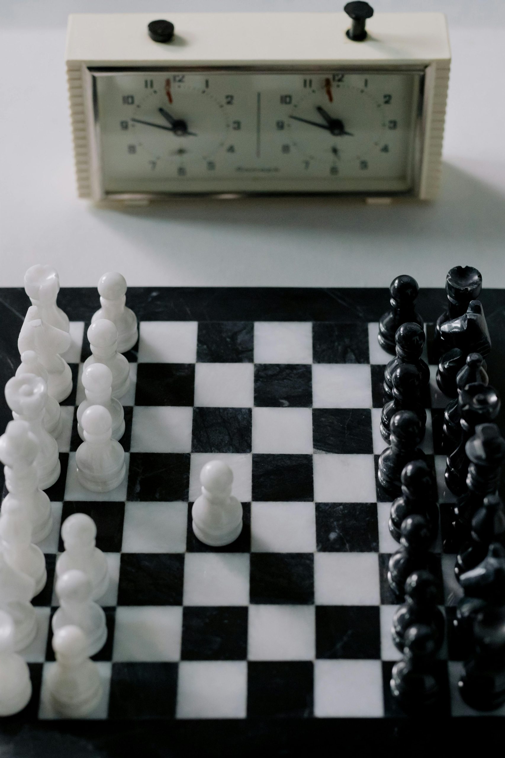Strategic chess game setup with black and white pieces on a marble board, featuring a classic chess clock.